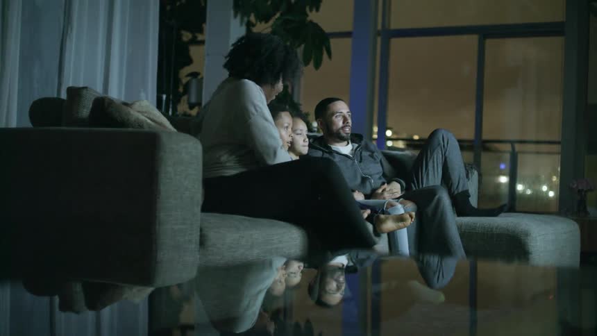 A man and woman sit down on the couch with their son and daughter to watch television