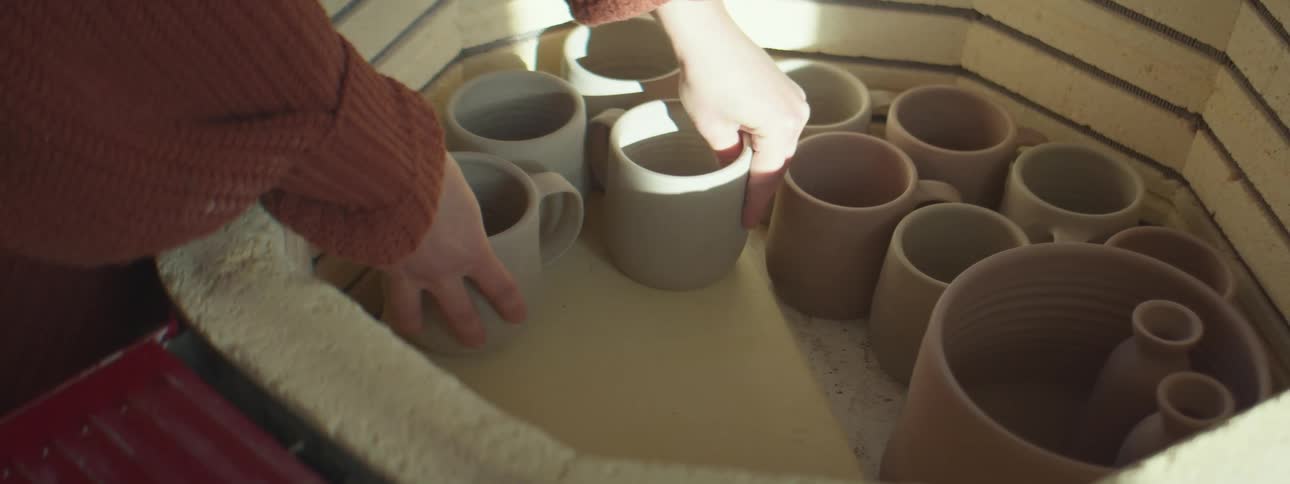 A woman places pottery pieces into a stone kiln