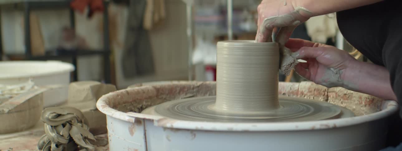 A person shaping wet clay on a spinning pottery wheel