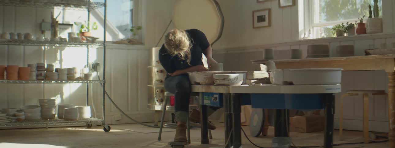 A woman shaping clay on a pottery wheel in a studio