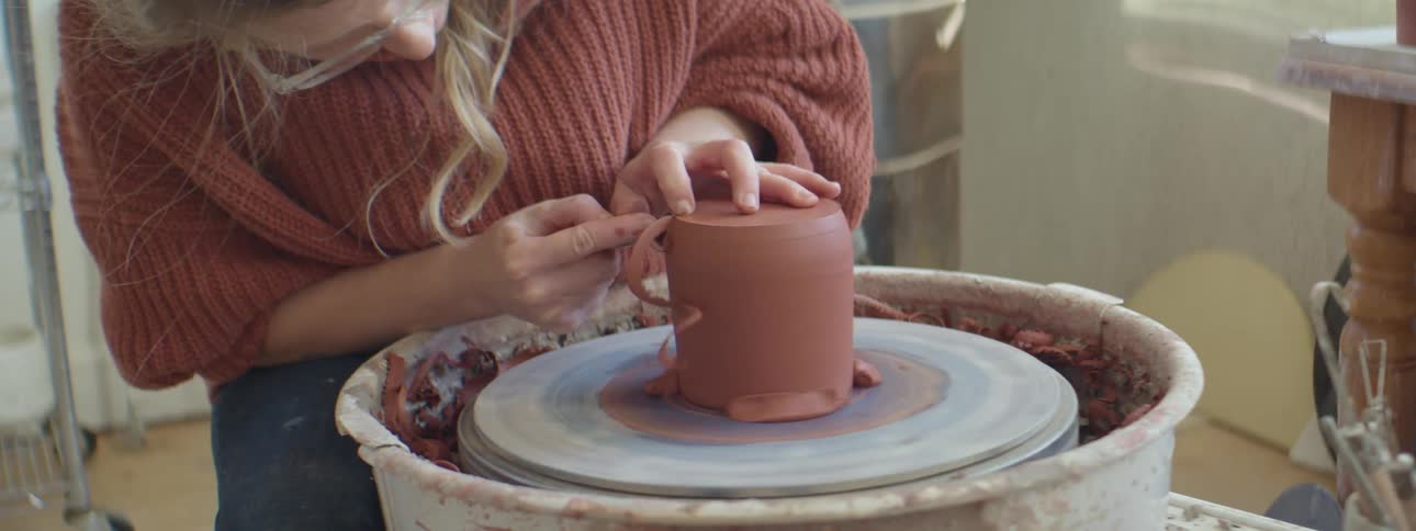 A woman shapes a piece of clay on a potters wheel