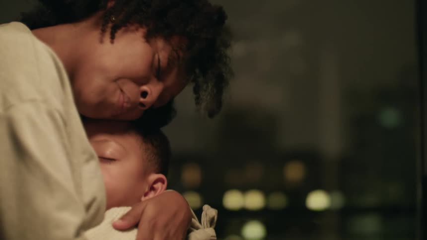 A woman in a room hugging a boy with a window in the background