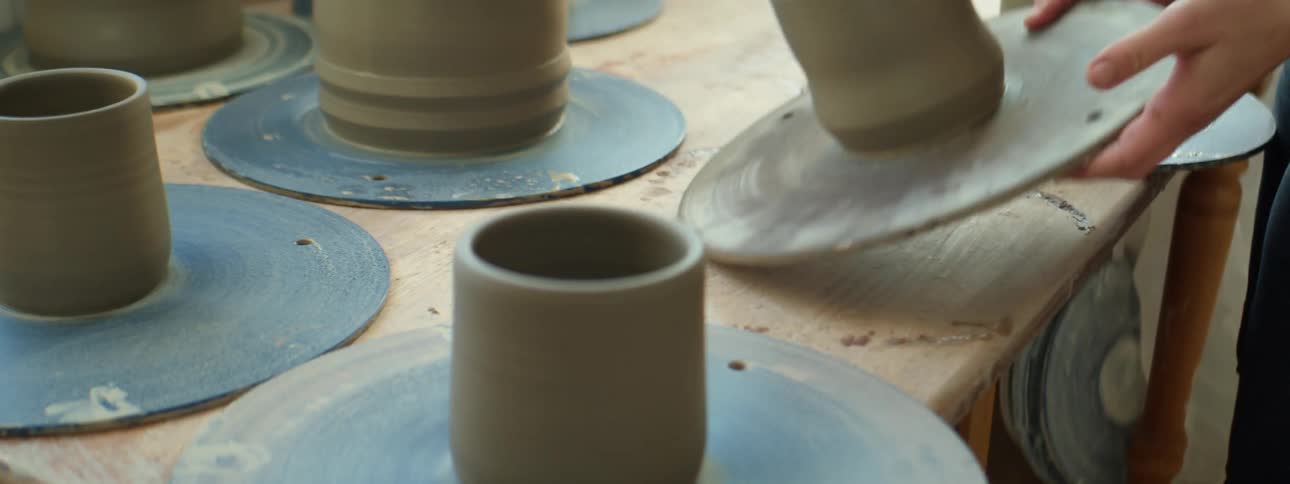 A person placing trays with fresh clay pottery over a table inside a workshop