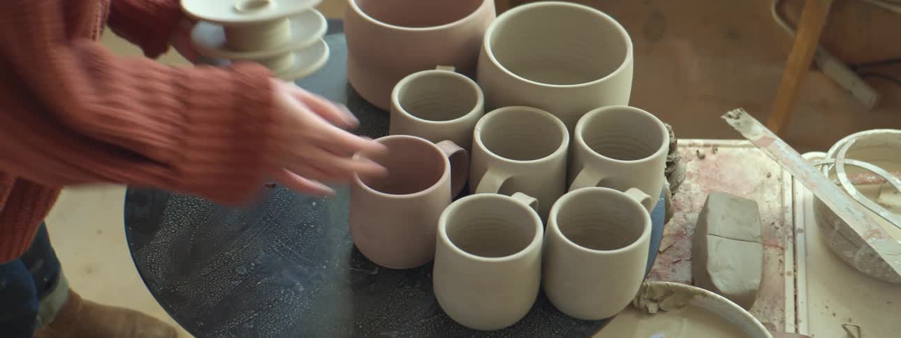 A person in a room placing mugs and saucers on a table