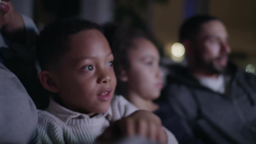 A mom smiles as she talks to her son while the whole family sits on the couch watching tv