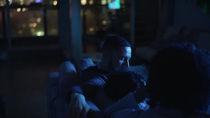 A man a girl and a woman sitting on a couch with windows in the background