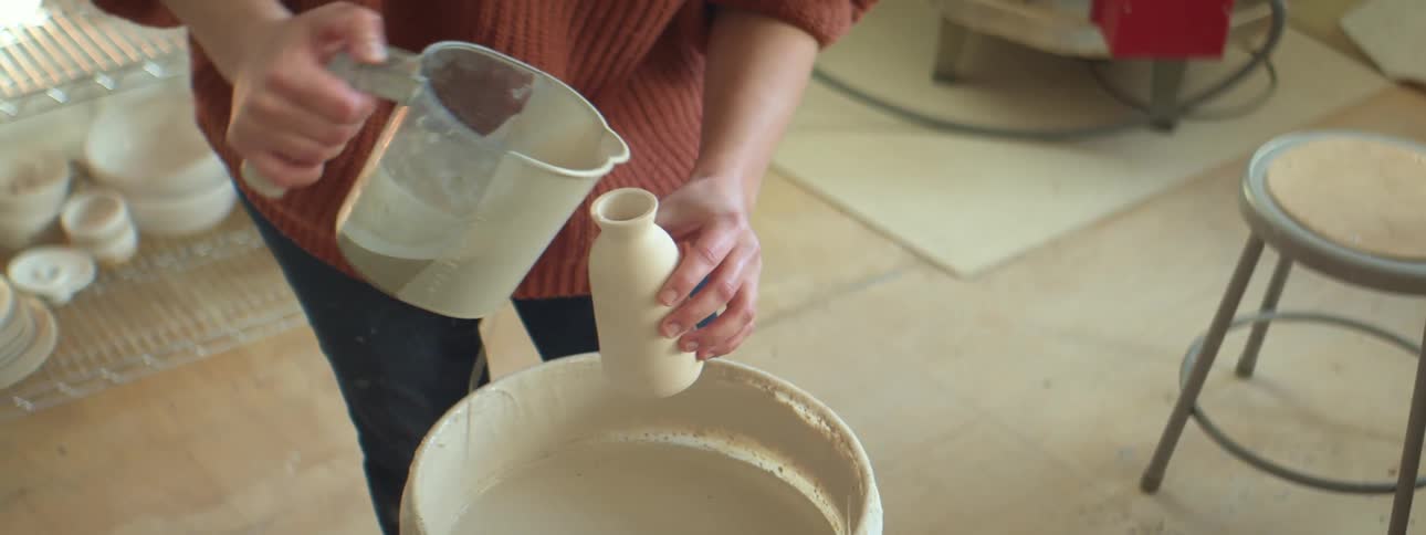 A woman pouring water into a clay vase in a pottery studio