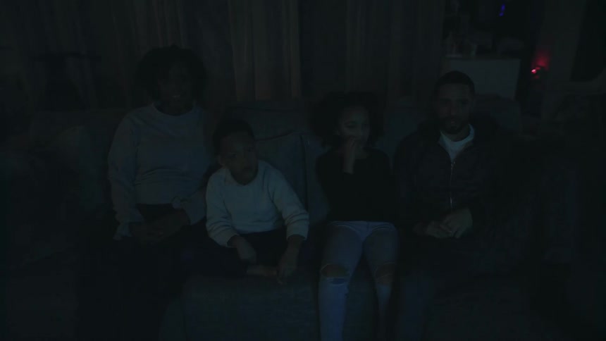A young family watching television on a sofa in a dark living room