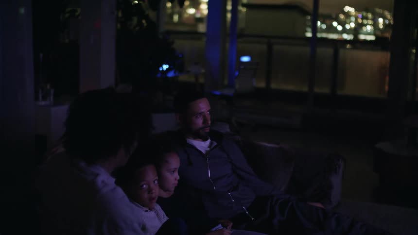 A man a woman a girl and a boy sitting on a couch with windows and plants in the background