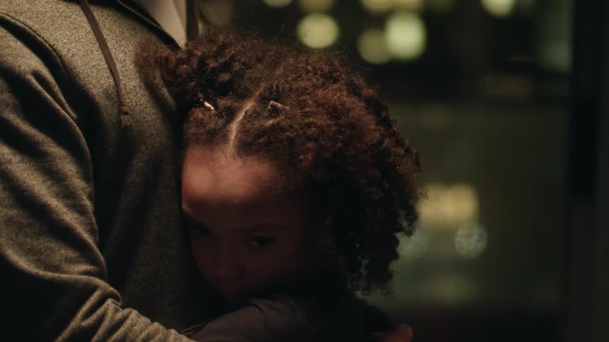 A girl looks up at her father as they slow dance in their city condo at night