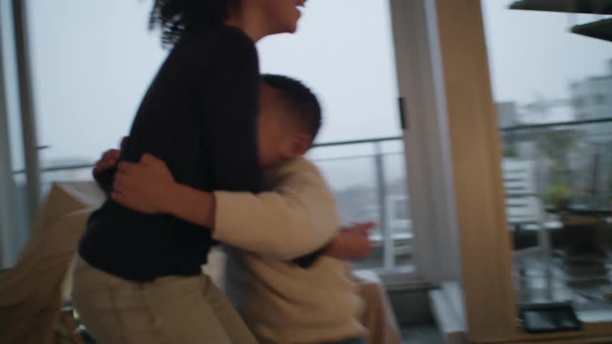 A little boy at home runs up to his sister who picks him up and swings him around