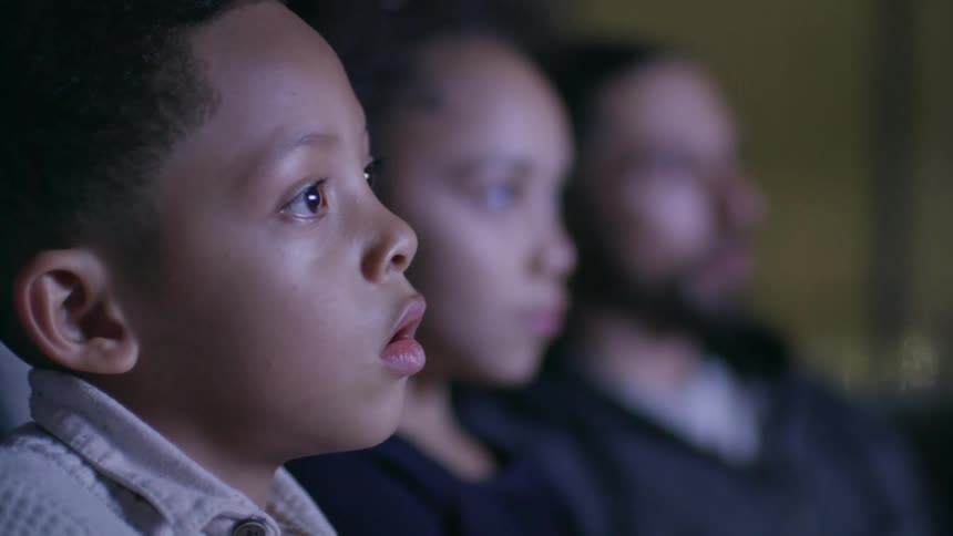 A father and two young children watching television on a living room sofa