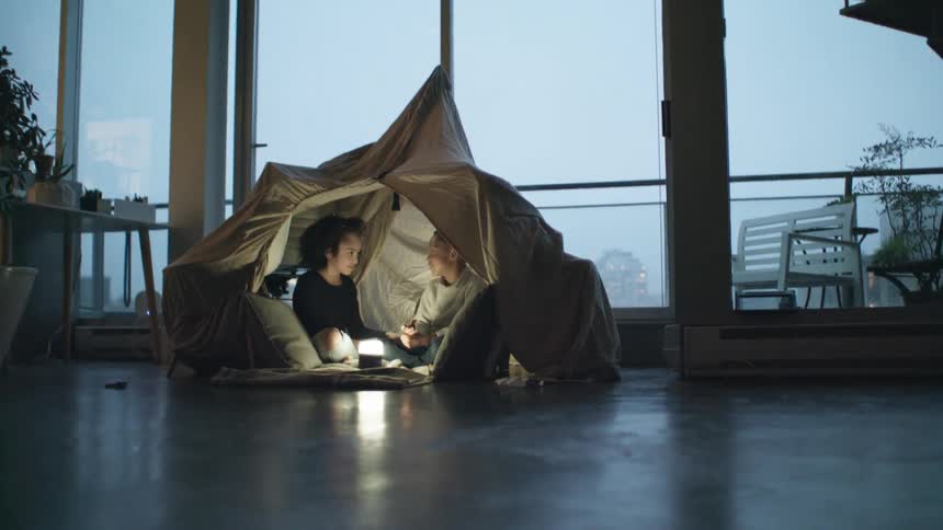 A young brother and sister sit in a fort in their home and talk