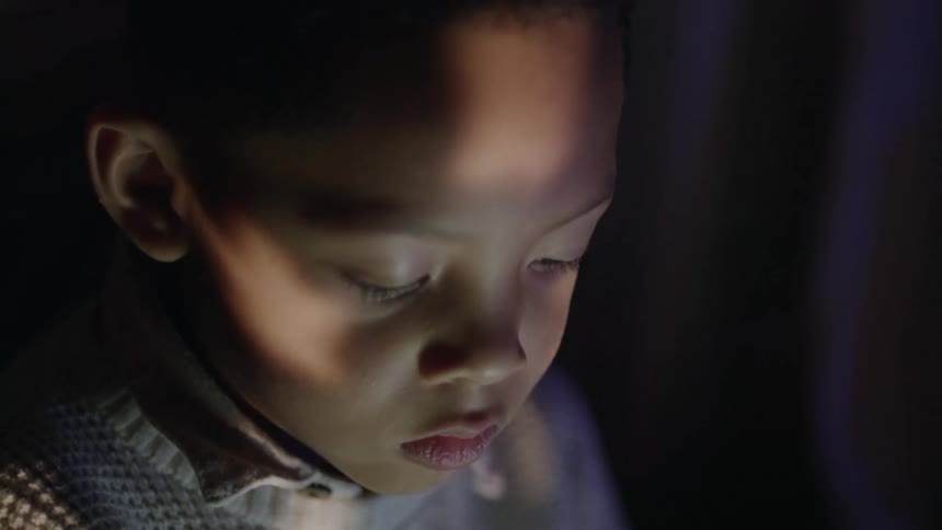 A young boy playing on a tablet in the dark
