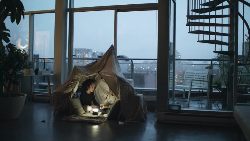 Two children sit together in a tent inside their home