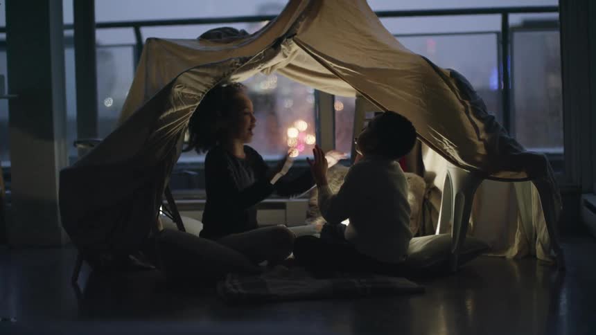 Young siblings playing clapping games inside a makeshift tent in the living room at home in the evening