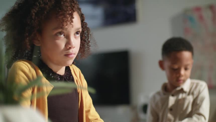 A boy climbs up and sits next to his sister in the family living room