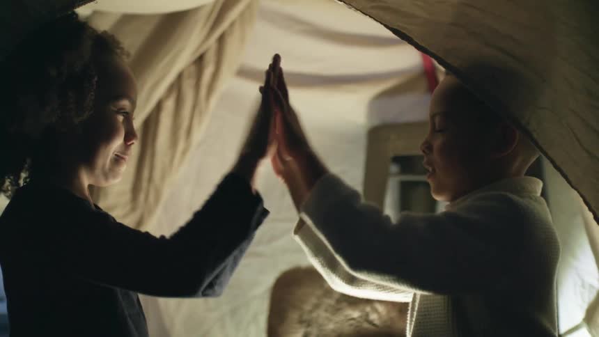 Brother and sister playing hand clapping games under a bed sheet tent at home