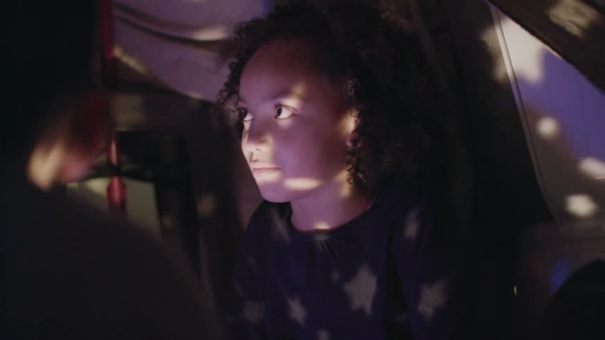 A girl and a boy in a tent with a light projector shining on their face