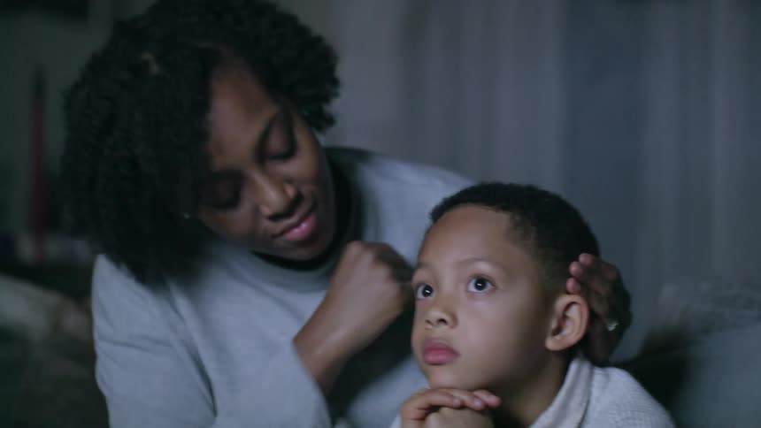 A woman sits on the couch with her children and kisses her son on the forehead and rubs his head