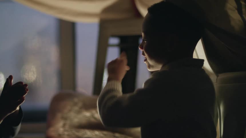 Siblings playing hand clapping games under a bed sheet tent in the bedroom at night