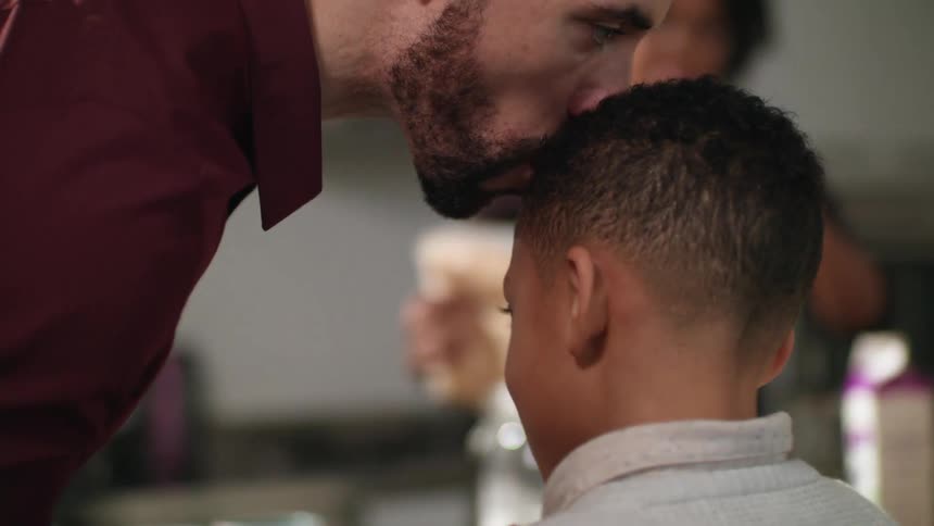 Father kissing his son in the forehead while the mother fixes breakfast in the kitchen