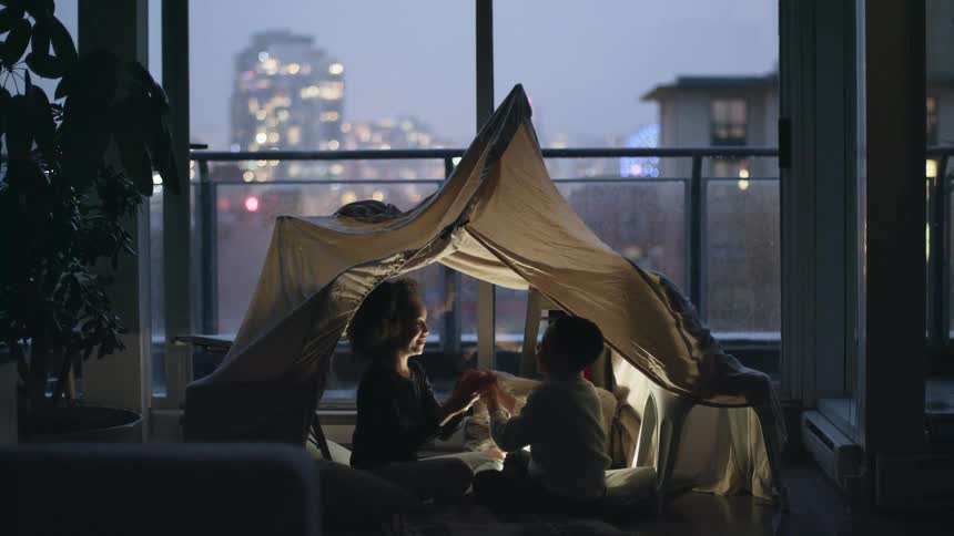 Siblings playing patty cake under a tent in living room at dawn