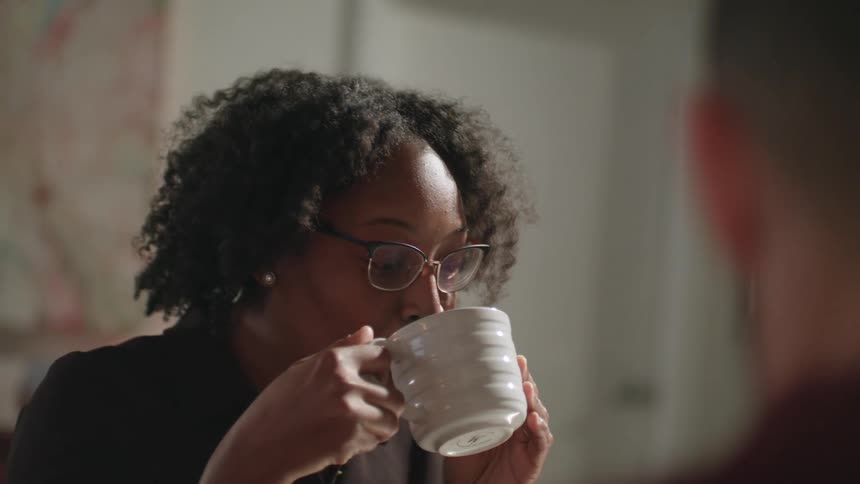 Young woman drinking a hot beverage in a cup talking to someone
