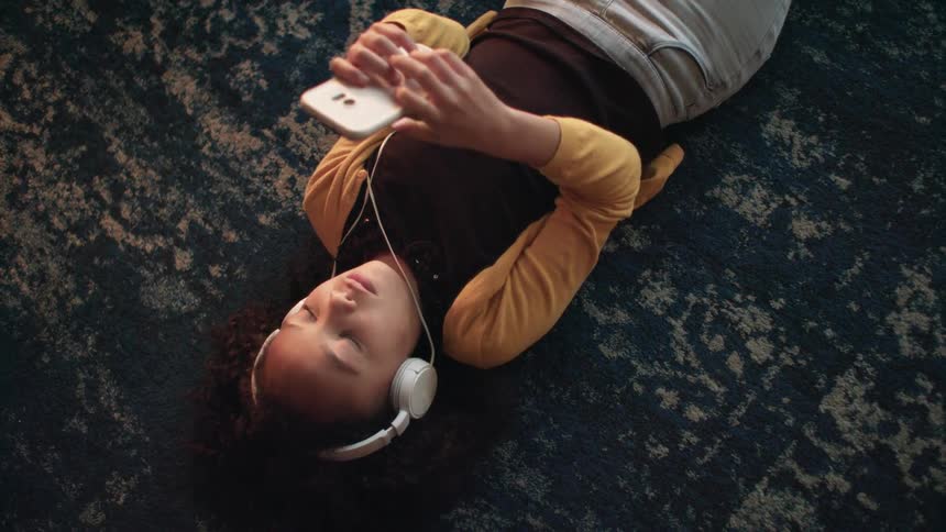 A child listening to music on a phone laying on the ground