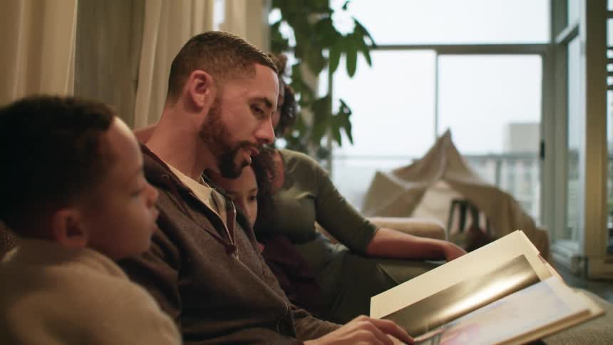 A man a woman a boy and a girl sitting on a couch looking at a book