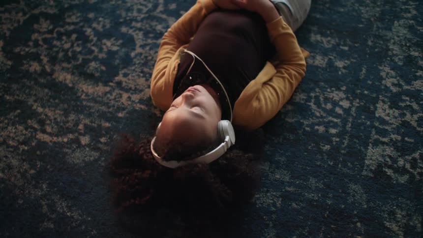 A young girl listening to headphones while lying on a blue rug