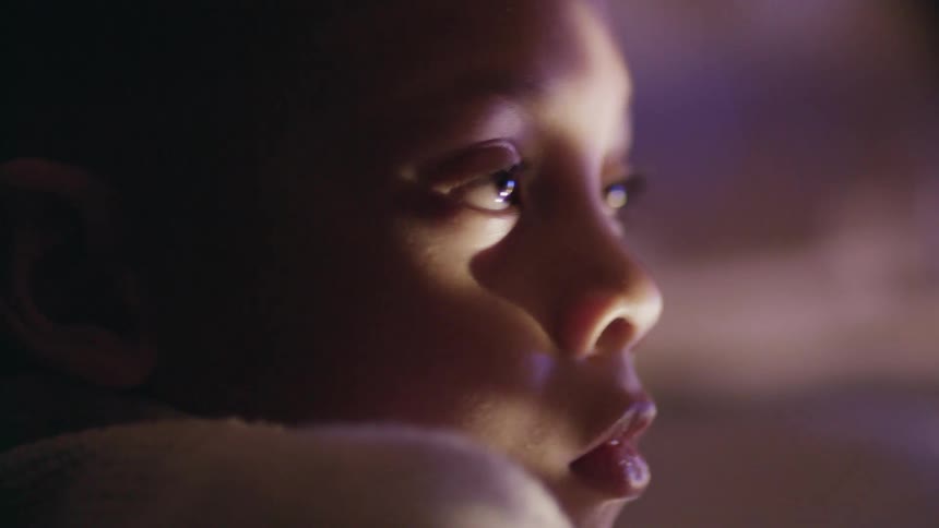 A young boy nodding and blinking in the dark