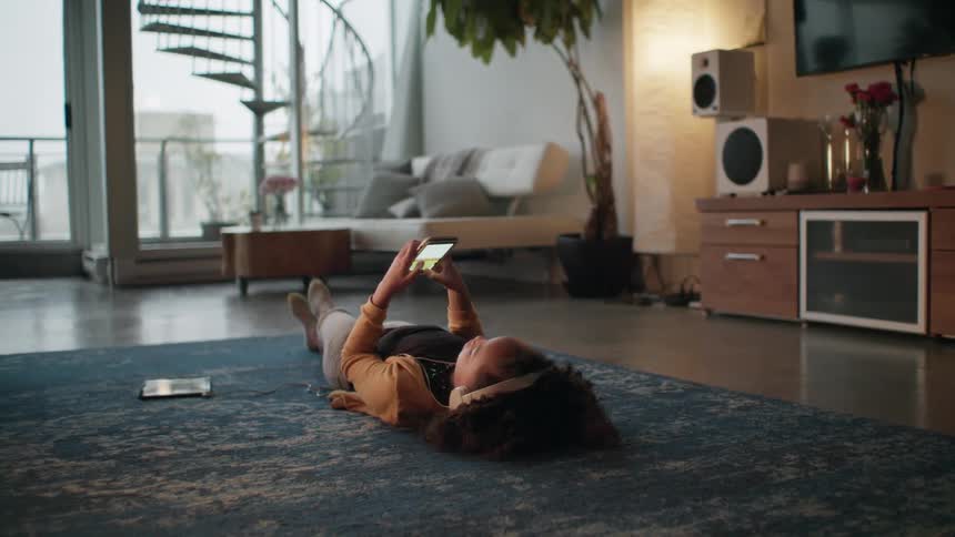 A young girl lies on the floor at her home and plays on a cell phone