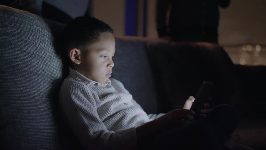 A boy sitting on a couch looking at a tablet