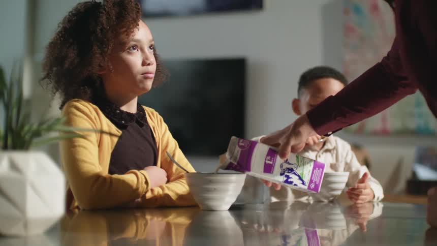 A father pouring milk into a bowl of cereal for his daughter