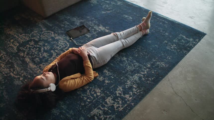 Young girl listening to music on a tablet using white headphones laying over the carpet on the living room