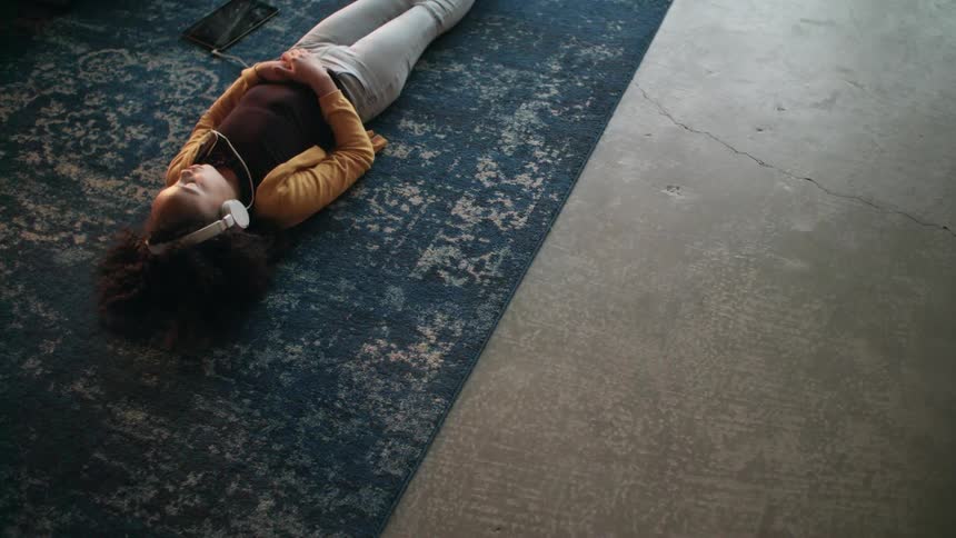 A woman lying on a rug listening to music through headphones attached to a tablet