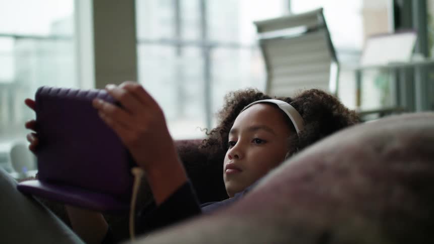 Young girl relaxing on bean bag watching a video on a tablet