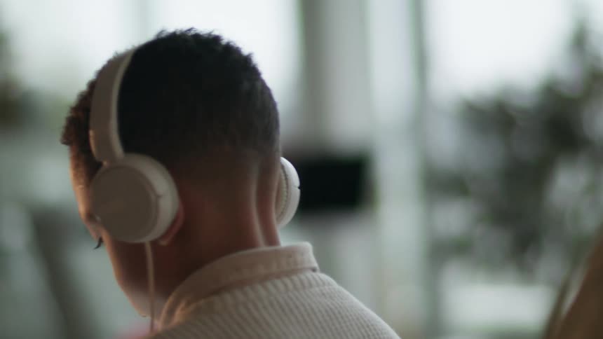 Young kid wearing white earphones sitting in the livingroom at home