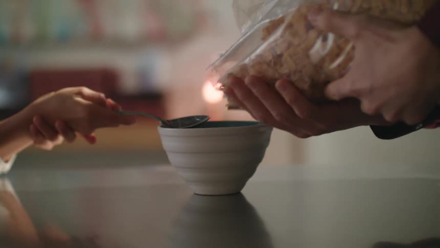 A boy impatiently waits for his father to pour cereal into a bowl