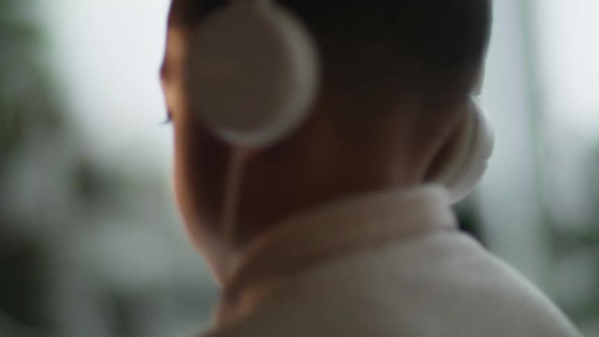 A boy in a room sitting on a couch looking at a tablet with headphones