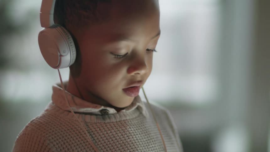 A young boy wearing headphones and holding a tablet indoors