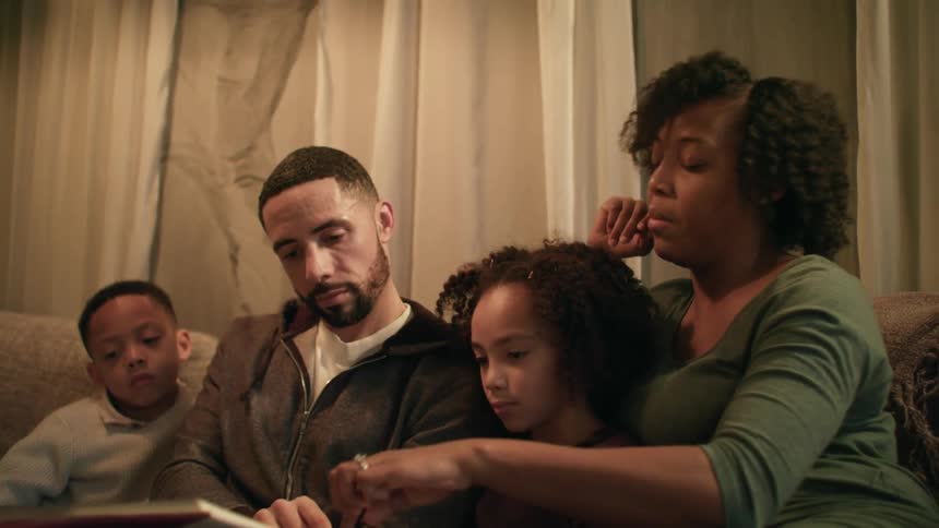 Family of four sitting in the couch on the living room reading a book