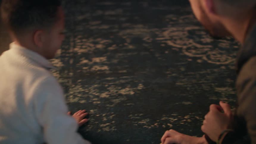 A man and a boy on a carpet on the floor playing with toy cars