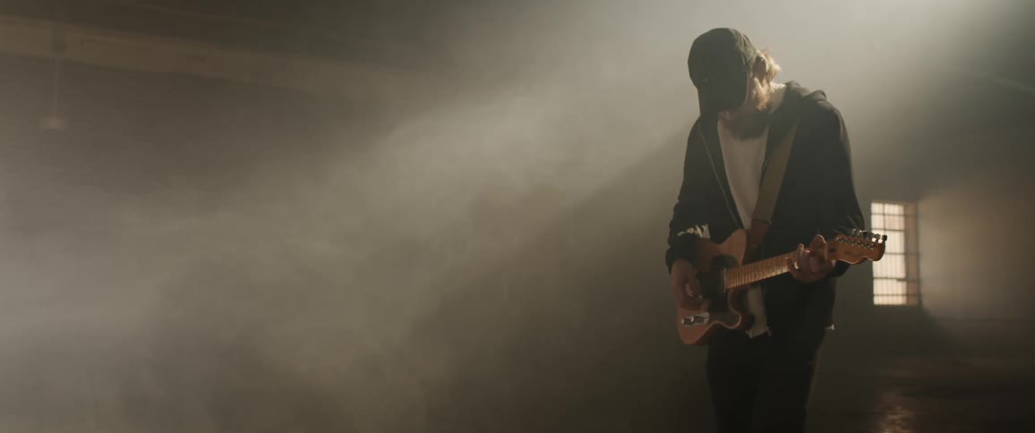Young man playing electric guitar inside a dimly lit room filled with white smoke
