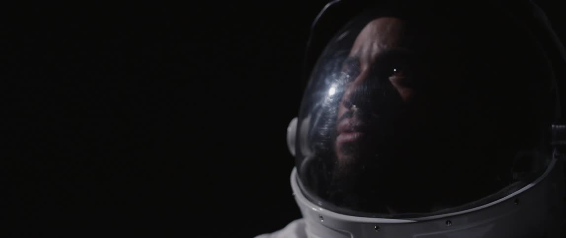 A man wearing a space helmet looks off into the distance