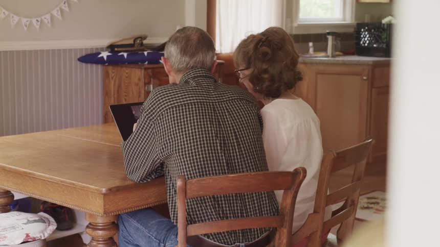 A man and a woman in a room sitting at a table with a wall and windows in the background