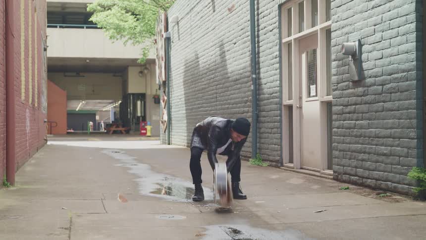 A man in a leather jacket smashing an acoustic guitar on concrete