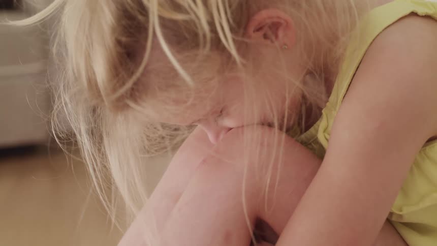 Young blonde girl sitting in the floor of the living room with her head over her knees