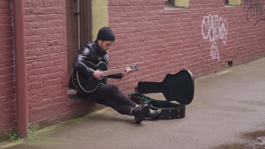 A man playing guitar sitting next to a guitar case